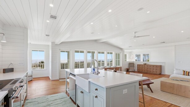 A spacious kitchen with a large island, wooden flooring, and a view of the ocean through large windows. - Luxury 5 Bedroom Beachfront Estate (Tybee Island)