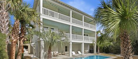 A two-story house with a pool, surrounded by palm trees and a clear sky.