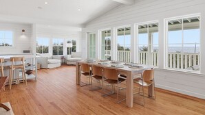 A spacious dining area with a wooden table and chairs, large windows with a view of the ocean, and a white interior. - Luxury 5 Bedroom Beachfront Estate (Tybee Island)