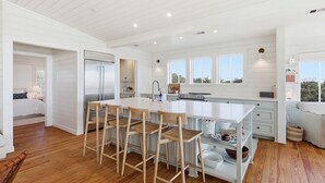 A spacious kitchen with a large island, wooden chairs, and a modern stove. - Luxury 5 Bedroom Beachfront Estate (Tybee Island)