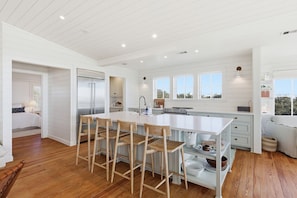 A spacious kitchen with a large island, wooden chairs, and a modern stove. - Luxury 5 Bedroom Beachfront Estate (Tybee Island)