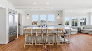 A modern kitchen with a large island, wooden chairs, and a built-in refrigerator. - Luxury 5 Bedroom Beachfront Estate (Tybee Island)