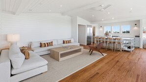 A modern living room with a sofa, coffee table, and a dining area with chairs and a kitchen in the background. - Luxury 5 Bedroom Beachfront Estate (Tybee Island)