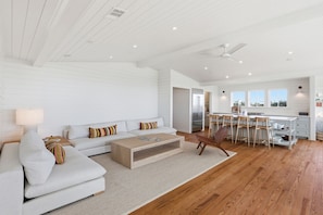 A modern living room with a sofa, coffee table, and a dining area with chairs and a kitchen in the background. - Luxury 5 Bedroom Beachfront Estate (Tybee Island)