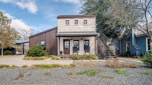 Un bâtiment à deux étages doté d’une façade en pierre, d’un revêtement extérieur en bois sur un des côtés et d’un escalier apparent menant au deuxième étage.