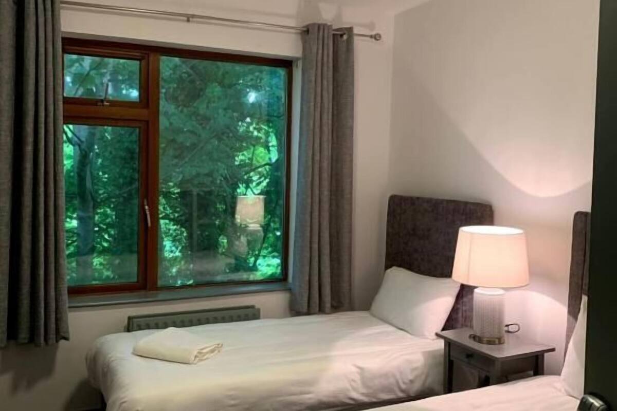 Una habitación de hotel con dos camas, una ventana con cortinas, una mesita de noche con lámpara y una luz en el techo.