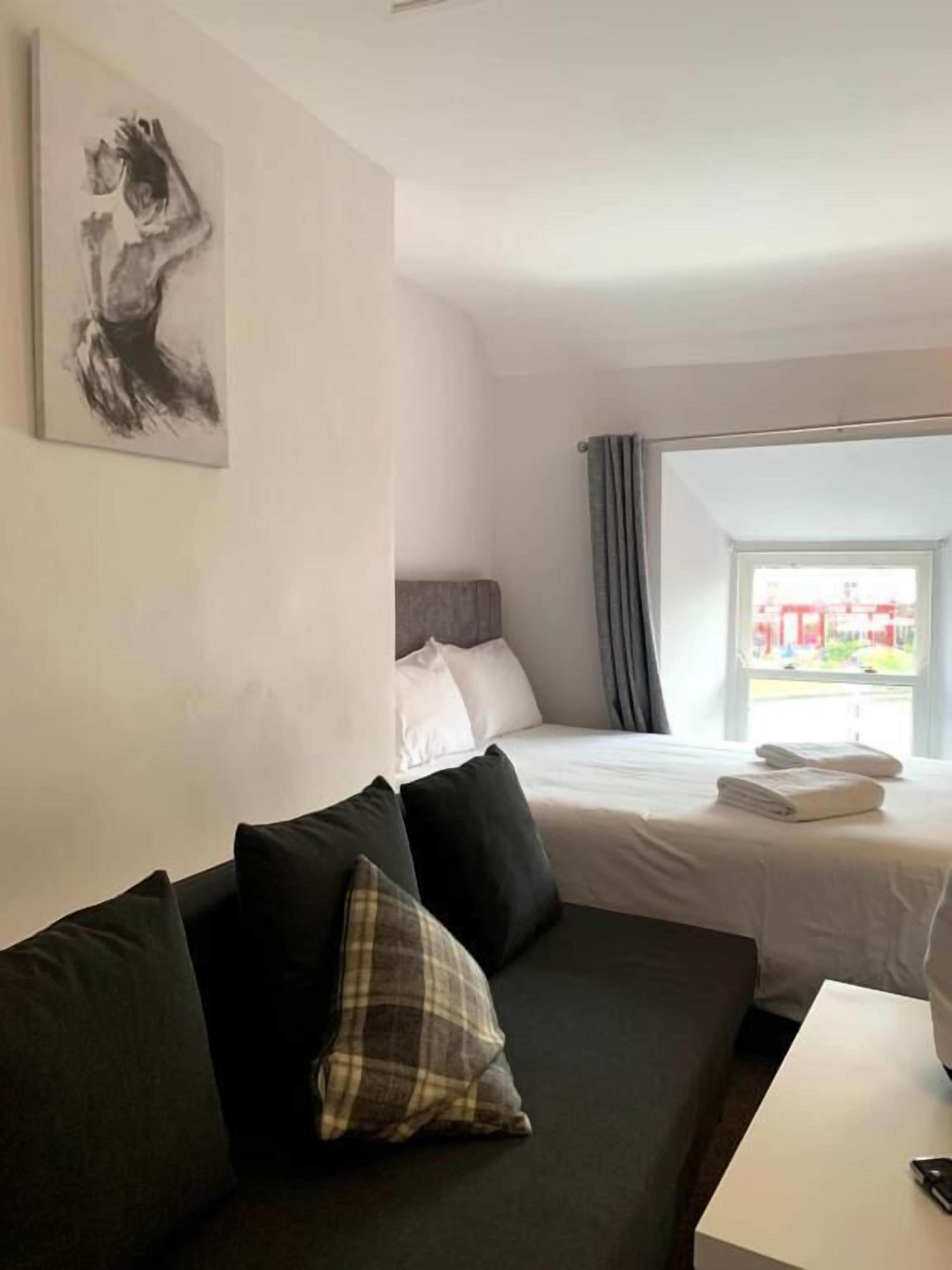 A hotel room with a bed, a sofa, a painting on the wall, and a window with curtains.