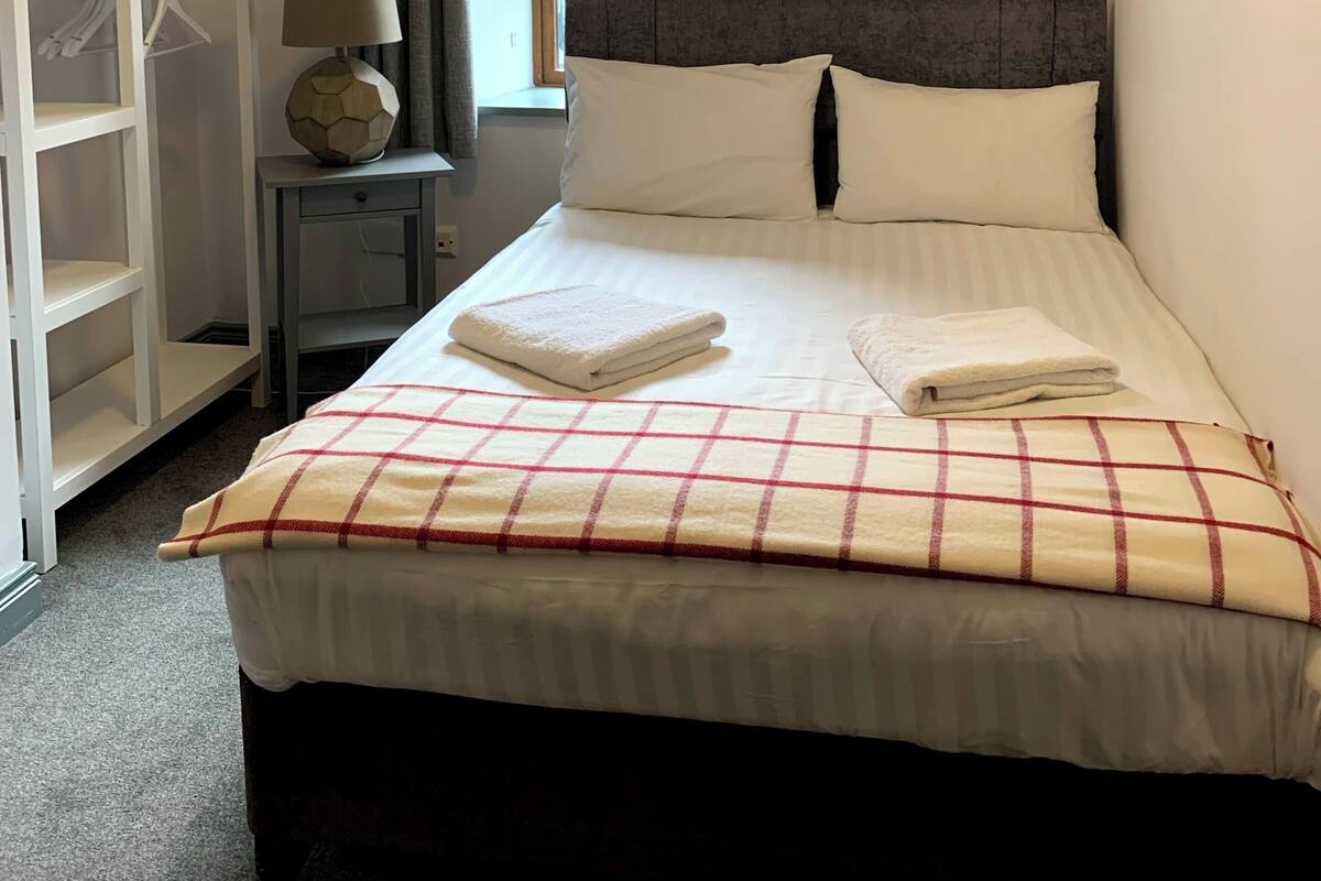 Habitación de hotel ordenada con cama, armario, mesita de noche y ventana con cortinas.