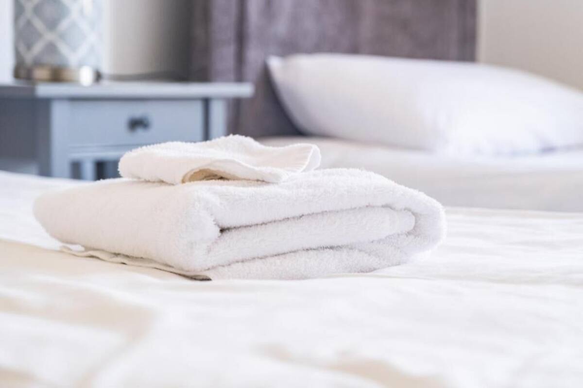 Una cama bien hecha con sábanas blancas y una toalla blanca doblada encima.
