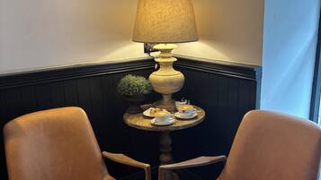 Een zithoek met twee leren stoelen, een bijzettafeltje met een lamp, een decoratieve wandversiering en een potplant.