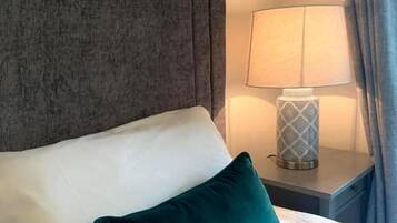 Una cama bien hecha con un cojín blanco y verde azulado, un cabecero gris y una lámpara de noche en una mesita.