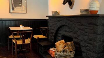Un interior acogedor con chimenea de piedra, sillas de madera, una mesa y una decoración de cabeza de venado montada en la pared.
