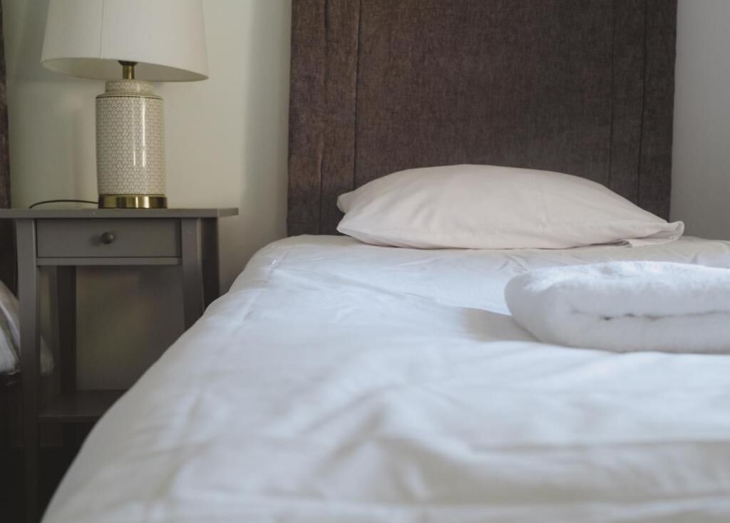 A neatly made bed with white linens and a pillow, a bedside table with a lamp, and a dark headboard.