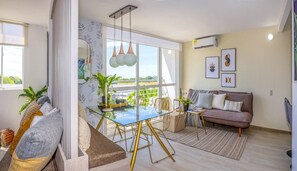 Una sala de estar moderna con una mesa de comedor de cristal, un sofá y un ventanal con vistas a zonas verdes.