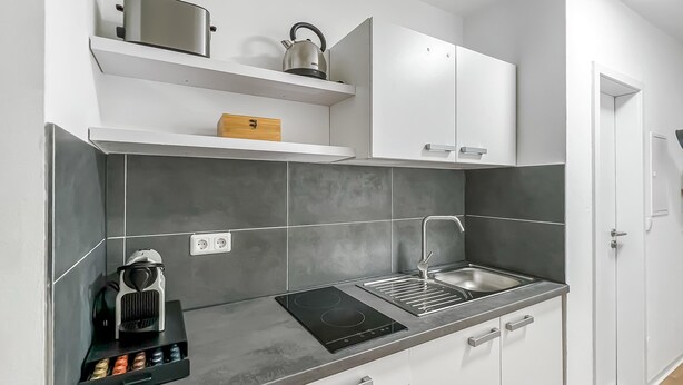 A modern kitchen with grey tiles, a kettle, a coffee maker, and a built-in stove. - Modern Studio Apartments in Nürnberg (Stein)