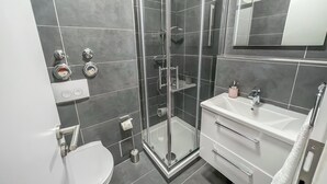 A modern bathroom with a glass-enclosed shower, a white sink, and a toilet. - Modern Studio Apartments in Nürnberg (Stein)