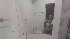 Ein Badezimmer mit weißem Waschbecken, Spiegel und Handtuchhalter. Es gibt eine Toilette und ein kleines Ablagebord mit gefalteten Handtüchern.