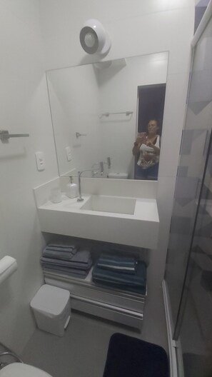 A bathroom with a white sink, mirror, and towel rack. There is a toilet and a small storage shelf with folded towels. - Cozy one-bedroom apartment, 1 block from the beach. Split air conditioning, 50" TV, sleeps up to 6 people. (Rio de Janeiro)