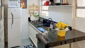 Eine kompakte Küchenzeile mit Kühlschrank, Herd, Spüle und einer kleinen Essecke mit zwei Hocker.