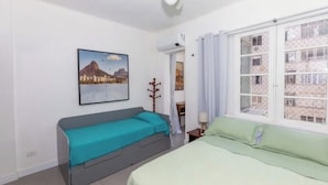 Ein Schlafzimmer mit einem Bett, einer Couch, einem Deckenventilator, einem Fenster mit Vorhängen und einem Bild an der Wand.