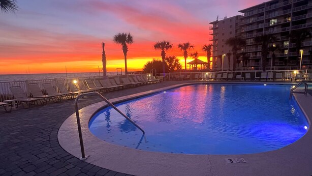 A swimming pool with a sunset view, lounge chairs, and a building in the background. - Gulf front 2-2 condo with indoor/ outdoor poo! Close to restaurants and shopping (Orange Beach)