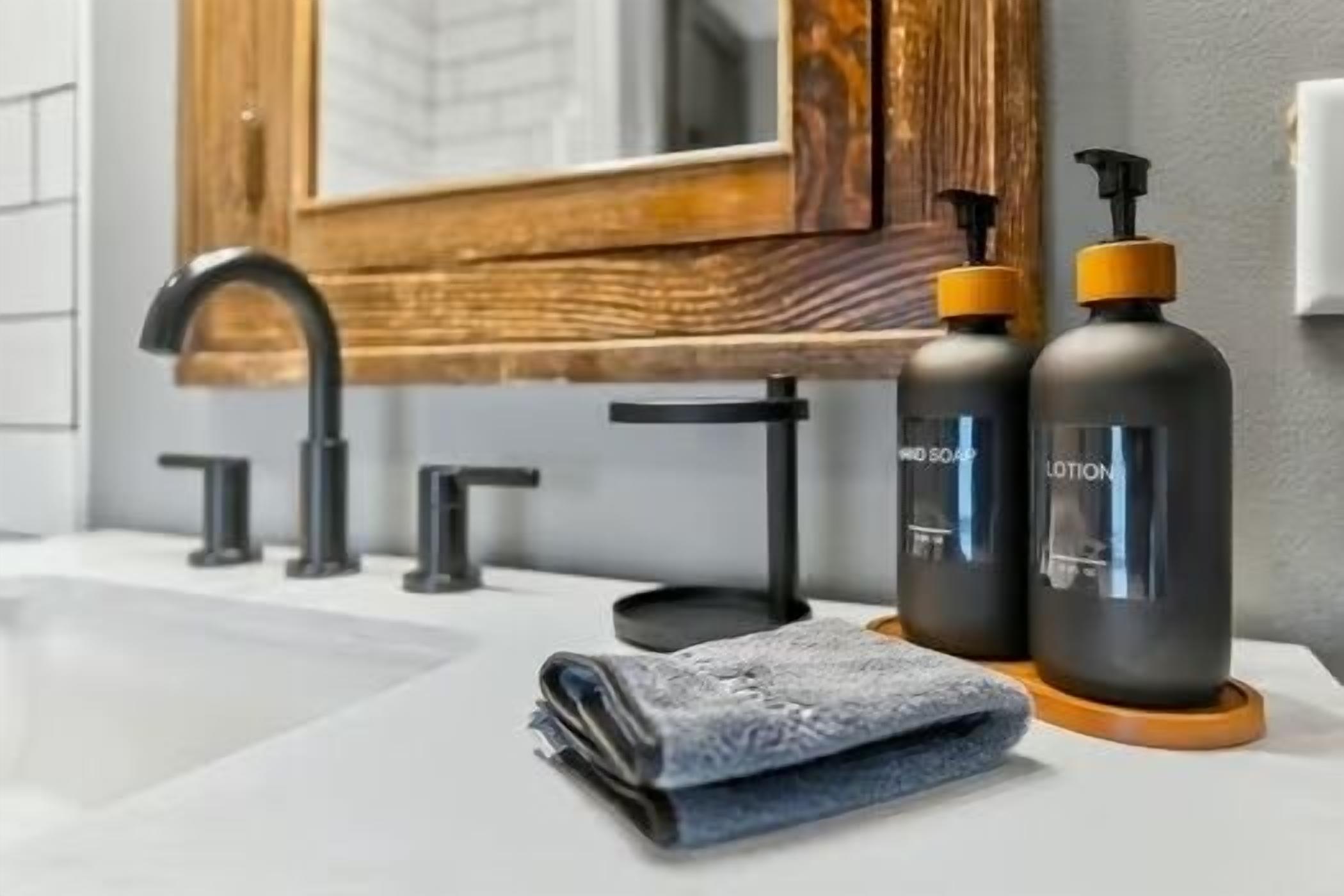 A bathroom with a modern sink, a wooden-framed mirror, and two bottles of lotion.