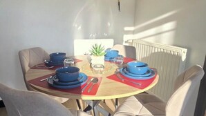 A dining area with a round table, four chairs, and a wall clock. - Quiet apartment Vittel - Near the thermal baths (Norroy)