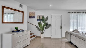 Un salon moderne avec un canapé blanc, un grand miroir, un escalier et une plante en pot.