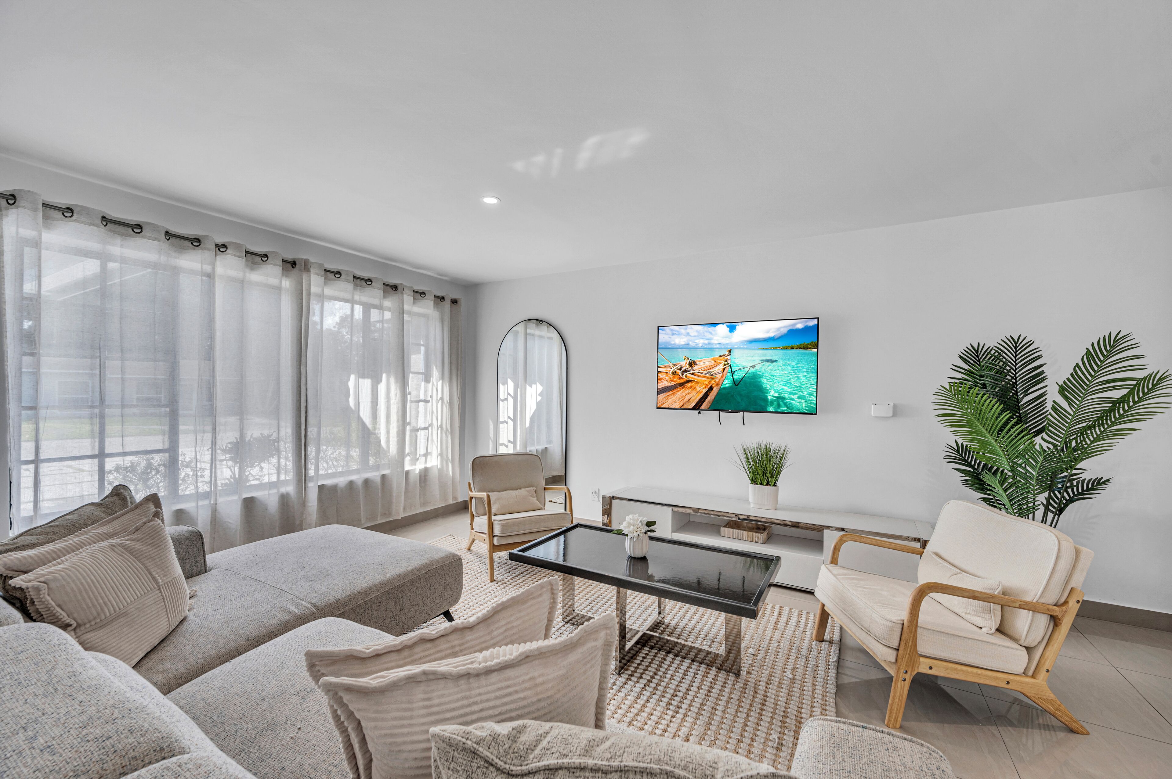 A modern living room with a sofa, armchairs, a coffee table, and a TV on the wall.