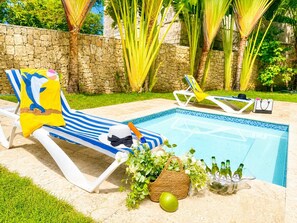 A poolside area with lounge chairs, a pool, and a stone wall. - 5 bd villa with rooftop in Sosua Ocean Village (Sosúa)