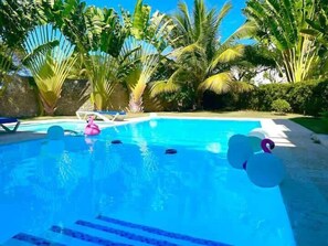 A swimming pool with clear blue water, surrounded by lush green palm trees and a stone wall. - 5 bd villa with rooftop in Sosua Ocean Village (Sosúa)