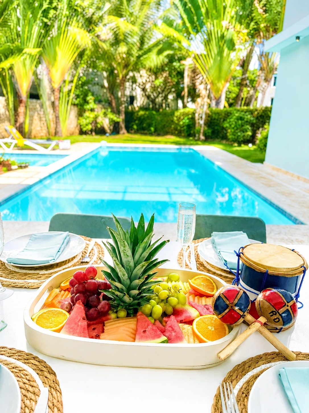 Een eettafel bij het zwembad, met een fruitschaal, een glas water en een drumstel.