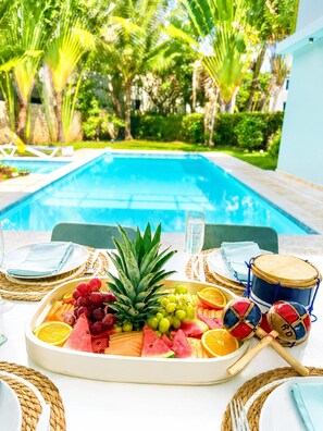 A poolside dining setup with a fruit platter, a glass of water, and a drum set. - 5 bd villa with rooftop in Sosua Ocean Village (Sosúa)