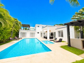 A modern pool area with a clear blue pool, lounge chairs, and a white building with large windows. - Villa Serena| 4 Suites, Pool, Terrace & Corner Lot (Sosúa)