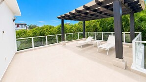 Een overdekt buitengebied met twee witte lounge fauteuils en een glazen balustrade.