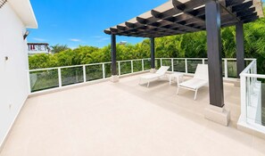 Ein überdachter Außenbereich mit zwei weißen Lounge-Stühlen und einem Glasgeländer.
