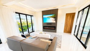 Ein modernes Wohnzimmer mit großem Flachbildfernseher, Kamin und Balkon mit Meerblick.