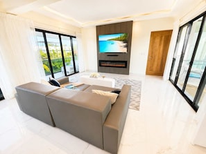 Uma sala de estar moderna com uma grande televisão de tela plana, lareira e varanda com vista para o oceano.