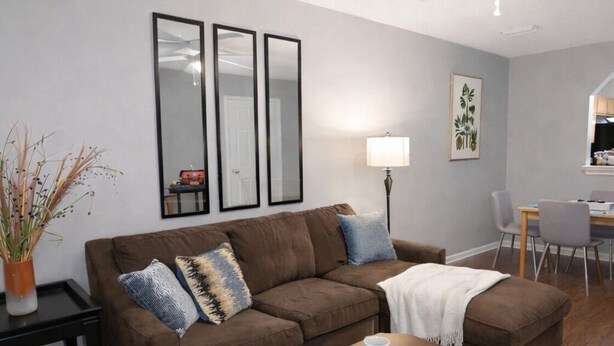 Un salon avec un canapé marron, une table basse, une lampe et un coin repas avec des chaises.