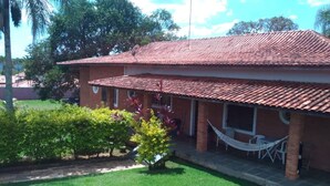 A two-story house with a tiled roof, a covered porch with outdoor furniture, and a small garden area with grass and shrubs.
