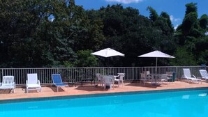 A swimming pool with lounge chairs and umbrellas, surrounded by a metal fence and trees.