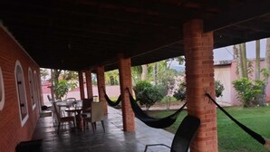 An outdoor covered patio with brick pillars, tables, chairs, and a hammock.