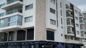 A multi-story building with balconies, a ground-level cafe, and a clear sky. - One-bedroom seafront apartment on Mackenzie with stunning sea views. (Larnaca)
