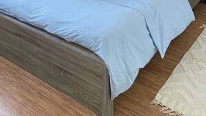 A neatly made bed with a blue bedspread, a wooden headboard, and a decorative wall piece. - One-bedroom seafront apartment on Mackenzie with stunning sea views. (Larnaca)