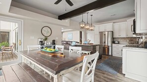 Cozinha moderna com armários brancos, geladeira de aço inoxidável e sala de jantar com mesa de madeira e cadeiras brancas.