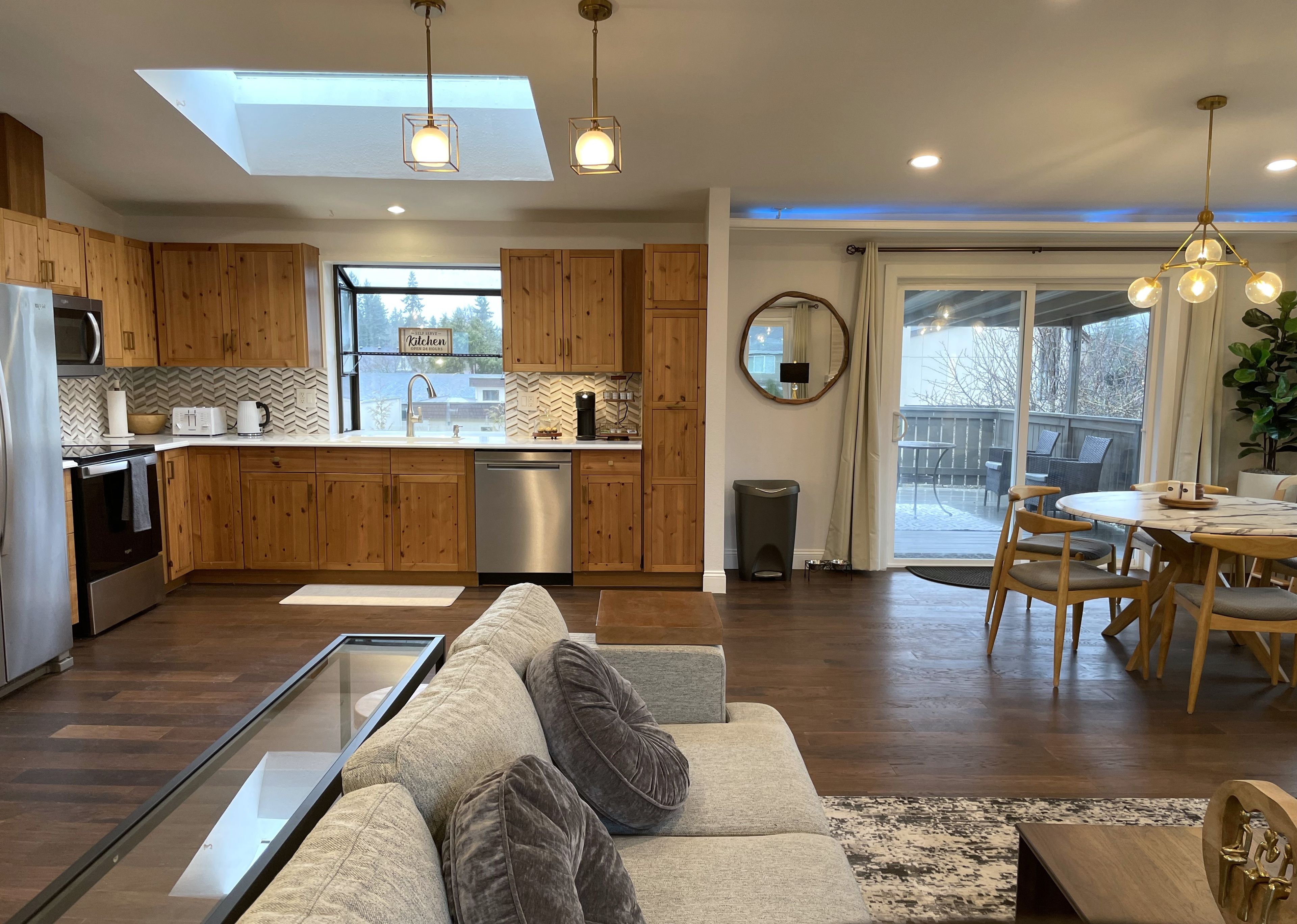A modern kitchen with wooden cabinets, a dishwasher, and a dining area with a round table and chairs.