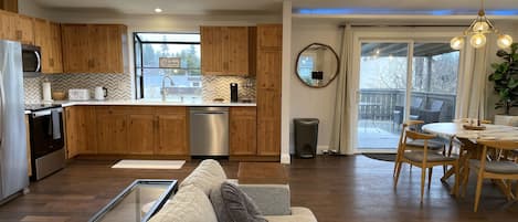 A modern kitchen with wooden cabinets, a dishwasher, and a dining area with a round table and chairs.