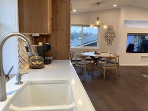A modern kitchen with a built-in sink, wooden cabinets, a coffee machine, and a dining area with a round table and chairs. - A Rather Posh 4 BR Renton Retreat with AC (Renton)