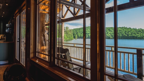 A room with large windows overlooking a lake, wooden deck, and a view of a forested area. - Private Adirondack Compound! (Saint Regis Falls)