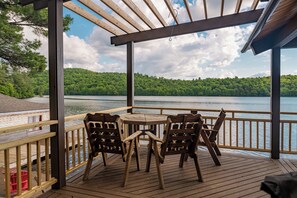A wooden deck with a table and chairs overlooking a lake with a forested shoreline. - Private Adirondack Compound! (Saint Regis Falls)